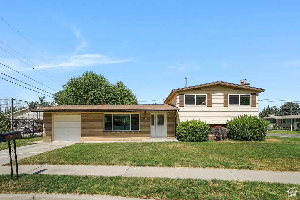 Split level home with a garage, concrete driveway, a front yard, and brick siding