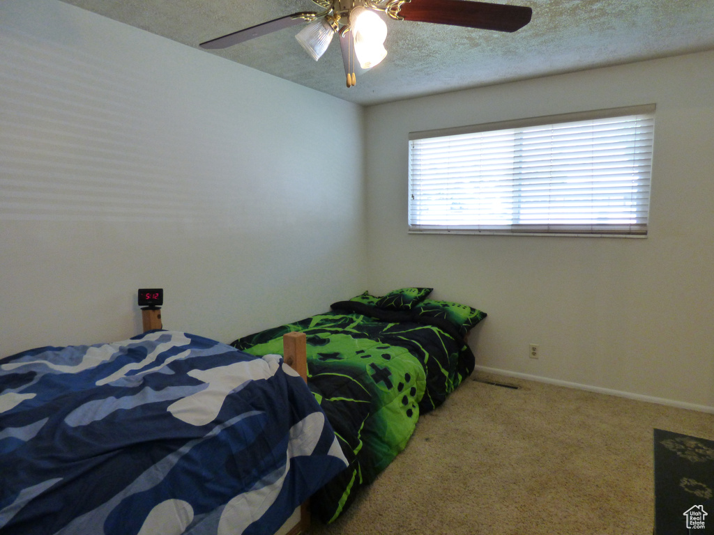 Bedroom with a textured ceiling, carpet flooring, ceiling fan, and baseboards