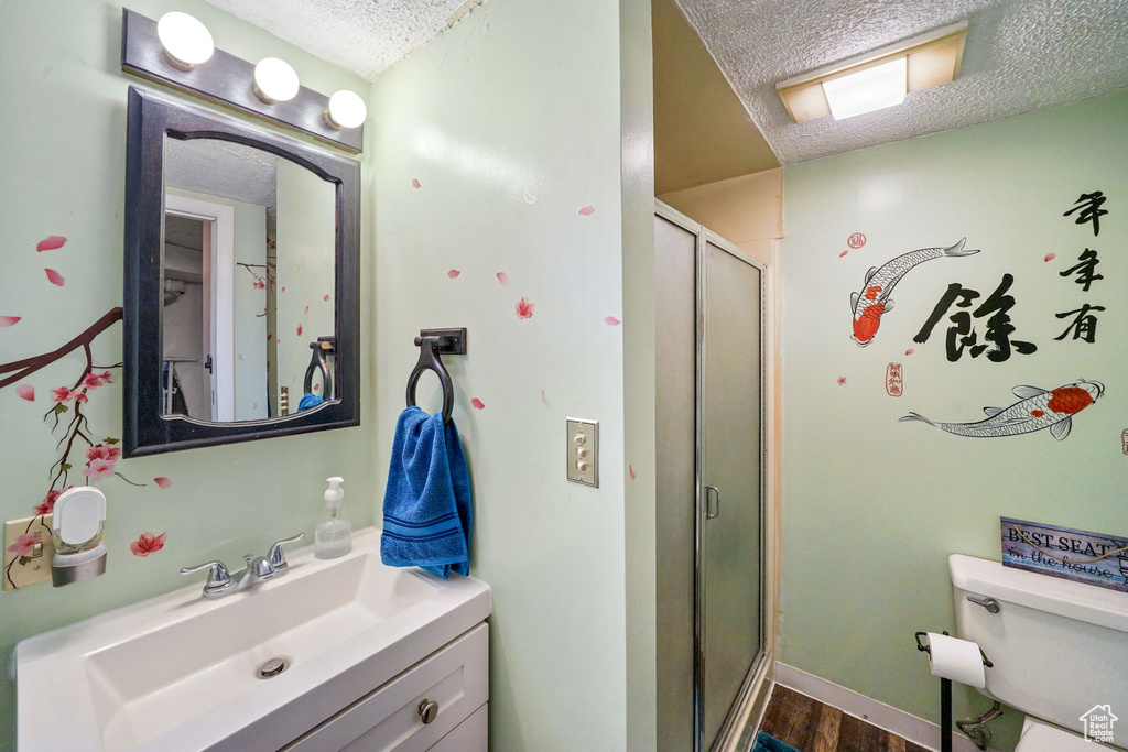 Full bath featuring a textured ceiling, vanity, a stall shower, and wood finished floors