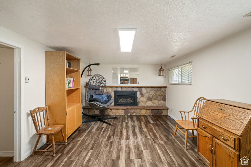 Living area featuring dark wood finished floors, a stone fireplace, and a textured ceiling