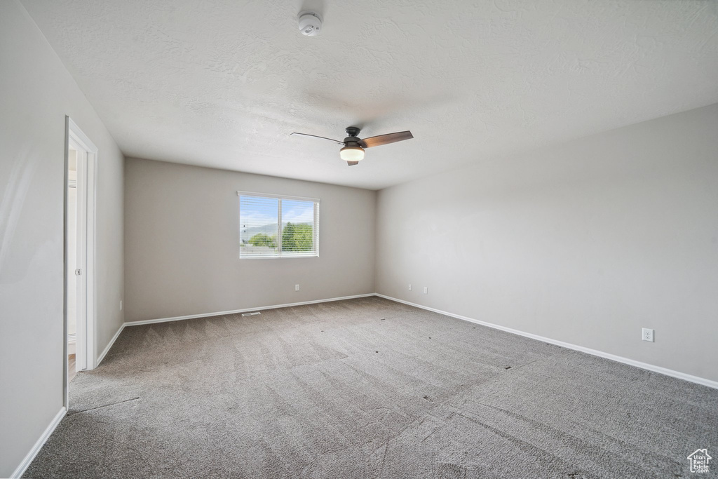 Carpeted spare room with ceiling fan, baseboards, a smoke detector, and a textured ceiling