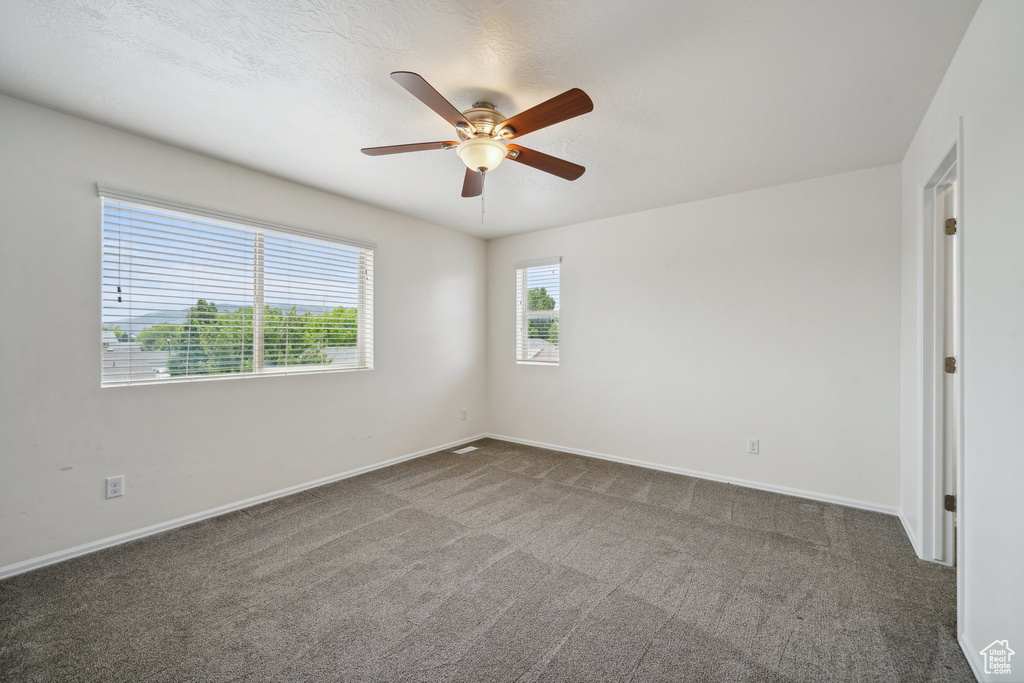 Unfurnished room with dark colored carpet, a ceiling fan, and baseboards