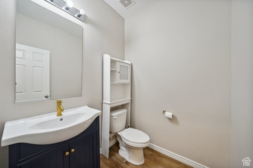 Half bathroom with wood finished floors, toilet, baseboards, vanity, and vaulted ceiling