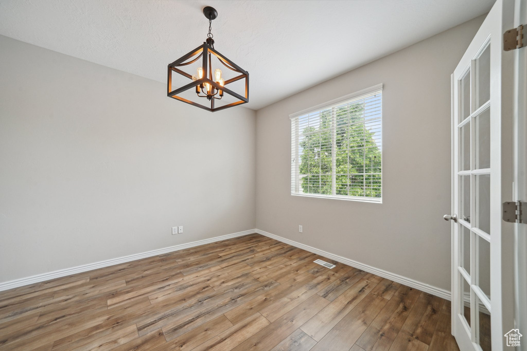 Unfurnished room featuring a chandelier, hardwood / wood-style floors, and baseboards