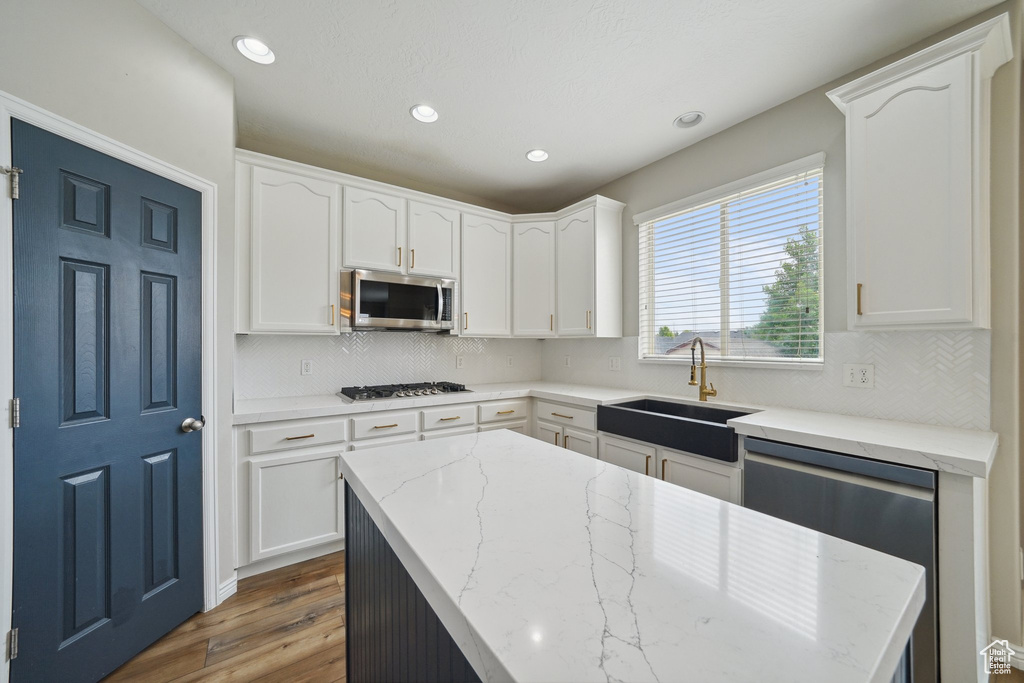 Kitchen with stainless steel appliances, a sink, wood finished floors, white cabinetry, and light stone counters