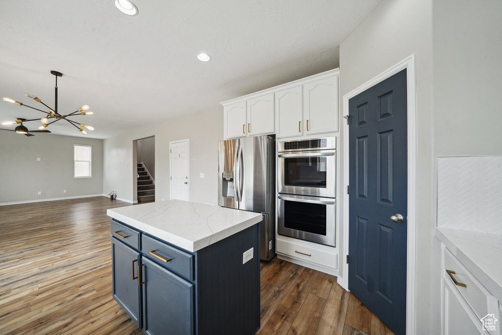 Kitchen featuring appliances with stainless steel finishes, a chandelier, dark wood finished floors, white cabinets, and a kitchen island