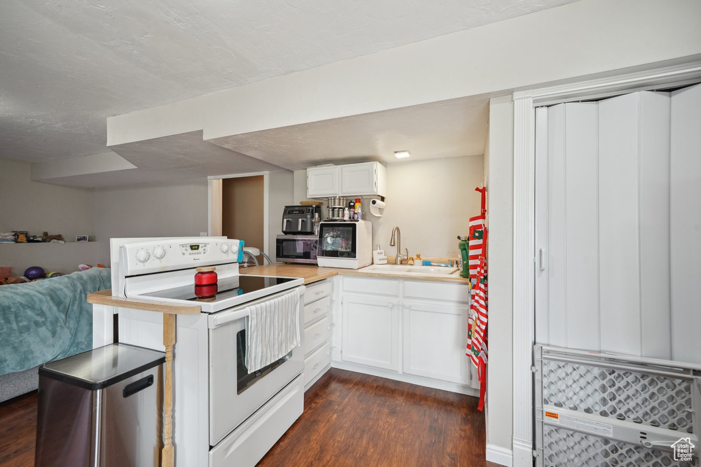 Kitchen featuring electric range, a sink, dark wood finished floors, white cabinets, and light countertops