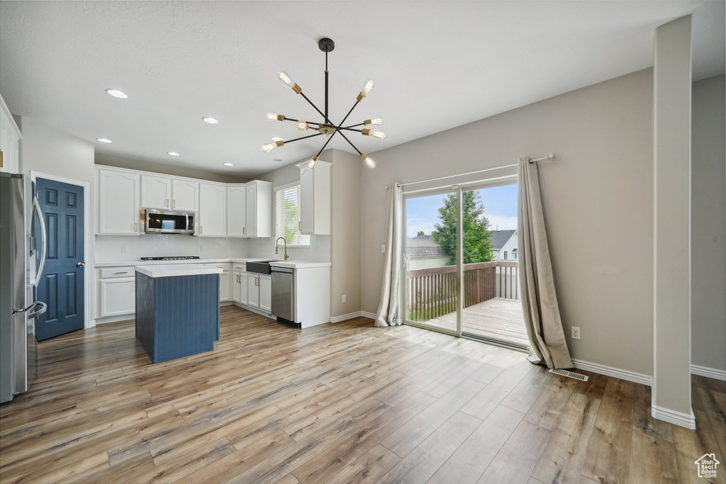 Kitchen with appliances with stainless steel finishes, a chandelier, white cabinets, light countertops, and light wood-type flooring
