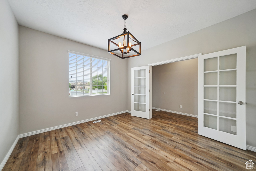 Empty room with french doors, a chandelier, hardwood / wood-style floors, and baseboards