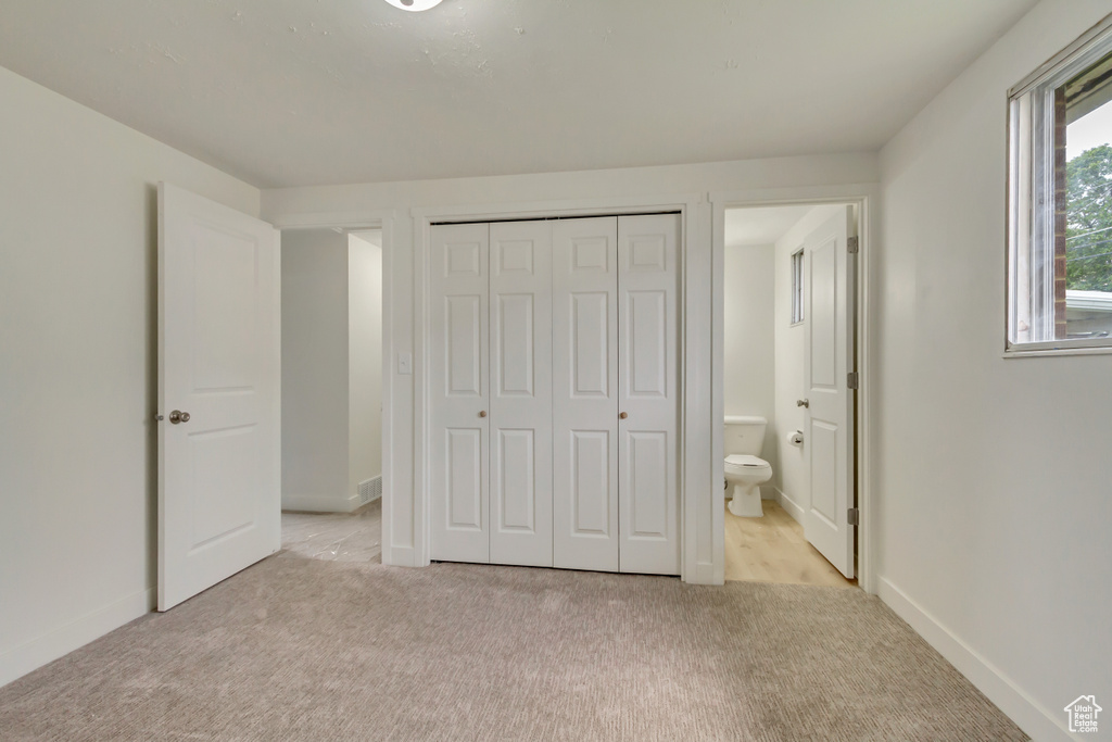 Unfurnished bedroom with light colored carpet, a closet, ensuite bathroom, and baseboards