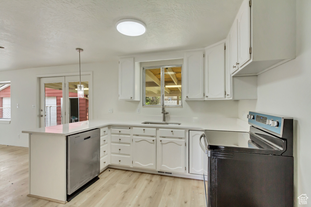 Kitchen with appliances with stainless steel finishes, a sink, a peninsula, light wood-style floors, and white cabinets