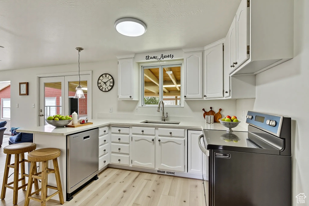 Kitchen featuring stainless steel appliances, a sink, a peninsula, light wood finished floors, and white cabinets
