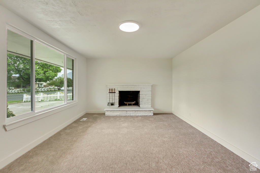 Unfurnished living room with carpet, a brick fireplace, and baseboards