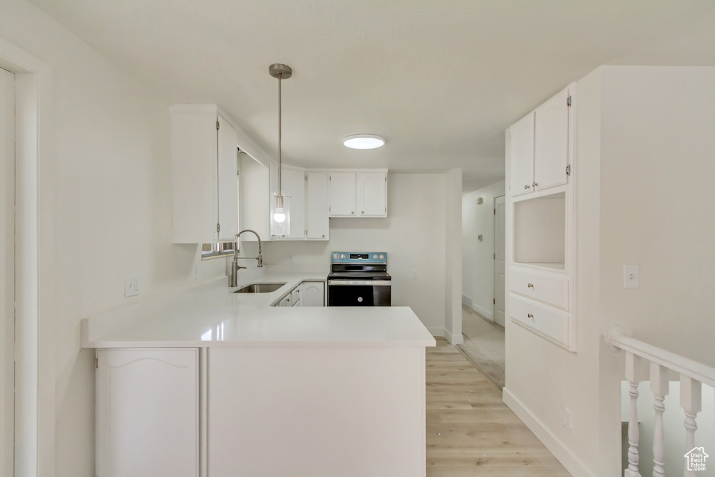 Kitchen featuring stainless steel electric stove, a sink, a peninsula, light wood-style floors, and light countertops