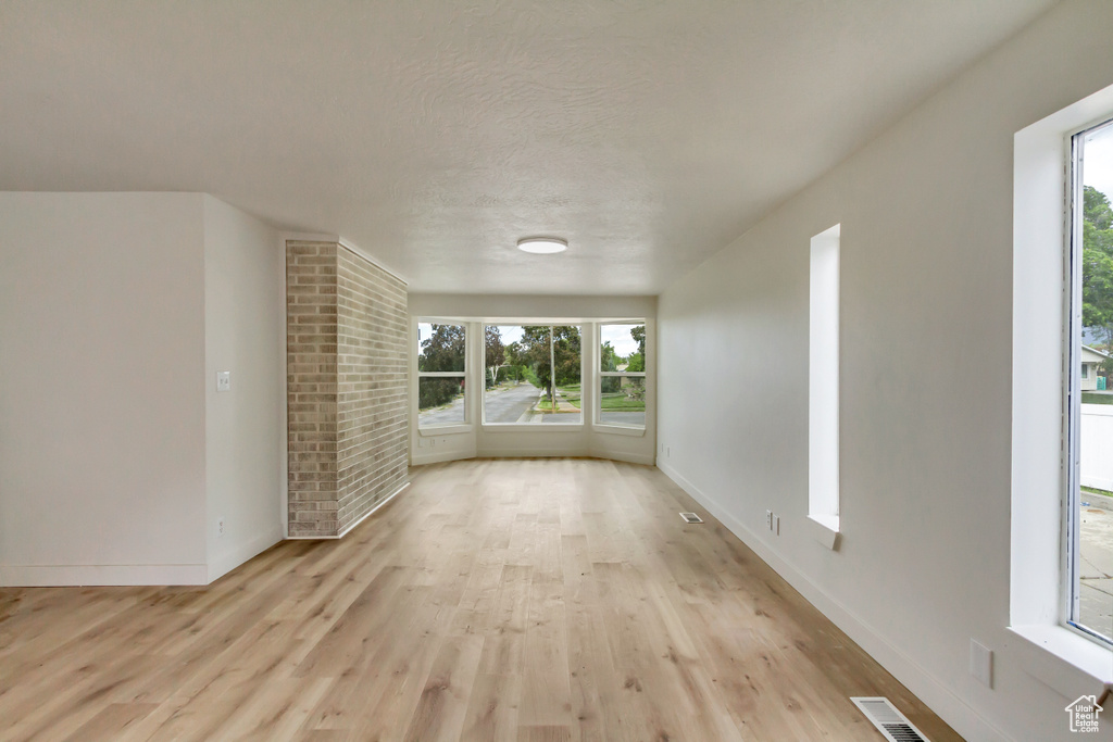Unfurnished living room with light wood-style floors, baseboards, and a textured ceiling