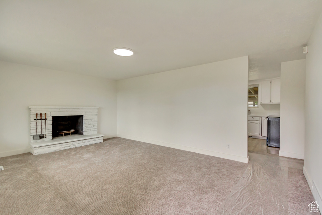 Unfurnished living room with light carpet, baseboards, and a fireplace with raised hearth