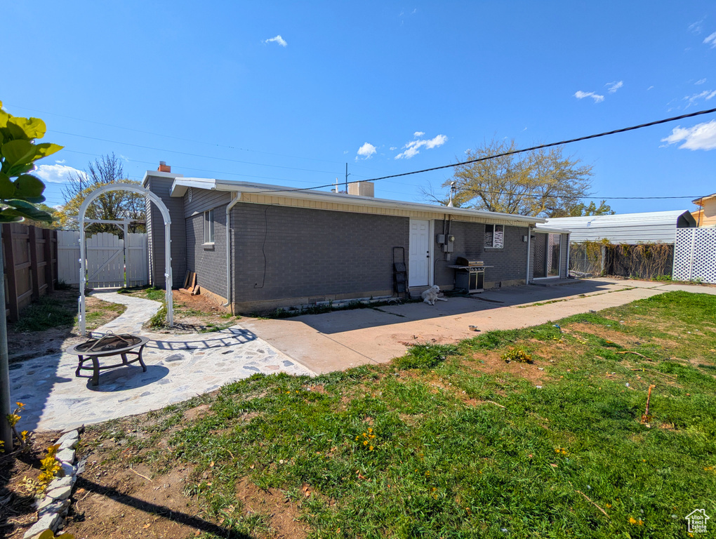 Back of property featuring a chimney, a fire pit, a patio area, brick siding, and a gate