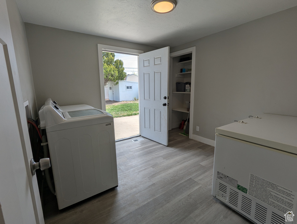 Laundry room with light wood-style flooring, separate washer and dryer, and baseboards