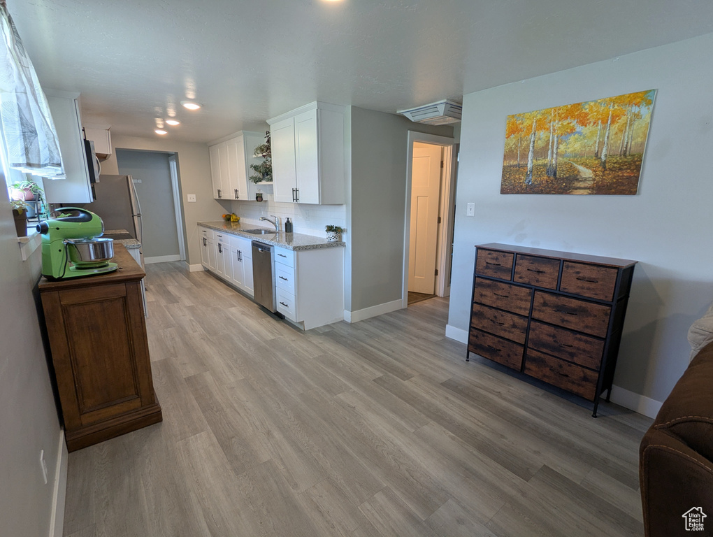 Kitchen featuring stainless steel dishwasher, baseboards, white cabinetry, and light wood finished floors