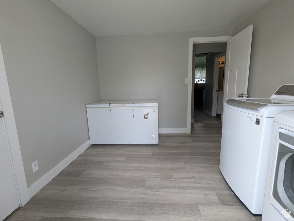 Laundry area with washer and clothes dryer, baseboards, and light wood finished floors