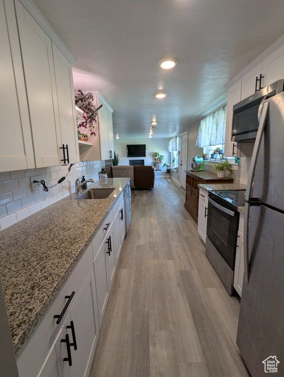 Kitchen with stainless steel appliances, a sink, light wood-style floors, and white cabinetry
