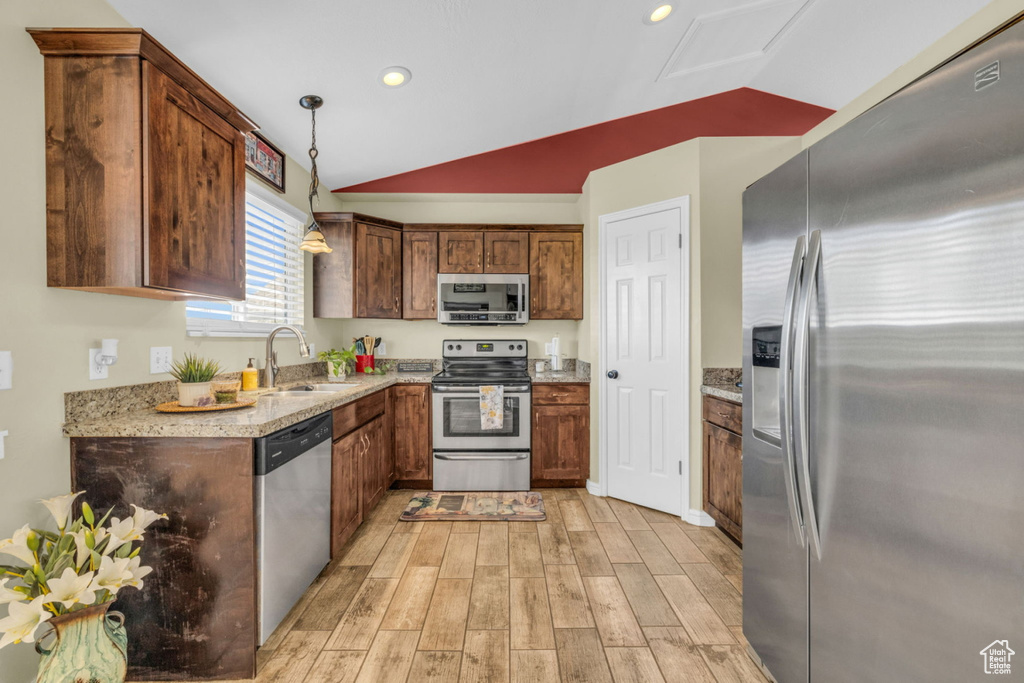 Kitchen featuring stainless steel appliances, a sink, light wood finished floors, lofted ceiling, and decorative light fixtures