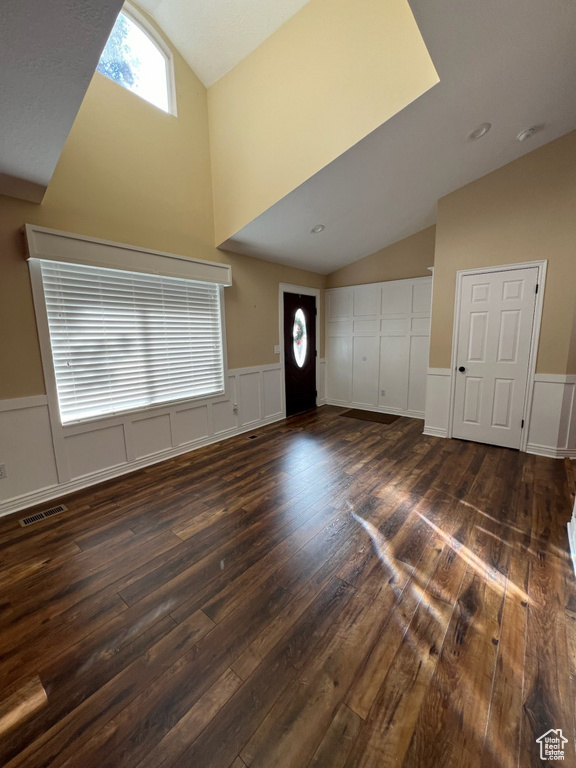 Foyer with vaulted ceiling, dark wood-type flooring, a decorative wall, and wainscoting