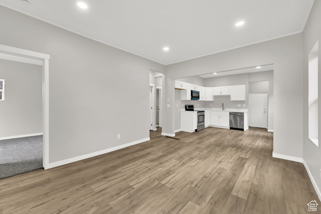 Unfurnished living room with baseboards, ornamental molding, light wood finished floors, recessed lighting, and a sink