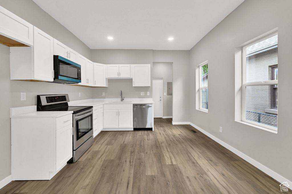 Kitchen with appliances with stainless steel finishes, a sink, baseboards, white cabinets, and recessed lighting