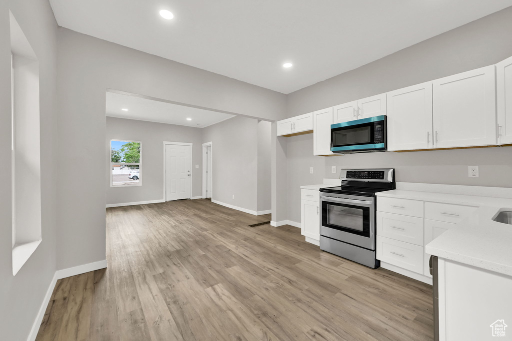 Kitchen with stainless steel range with electric cooktop, light countertops, white cabinets, light wood-style floors, and recessed lighting