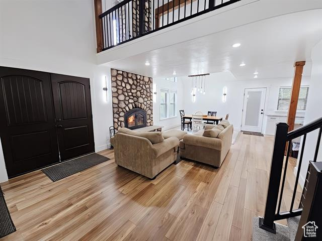Living area featuring light wood-style floors, ornate columns, a stone fireplace, a towering ceiling, and baseboards