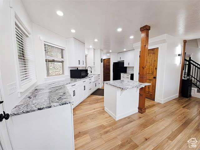 Kitchen featuring black appliances, white cabinetry, a kitchen island, light stone counters, and a breakfast bar area