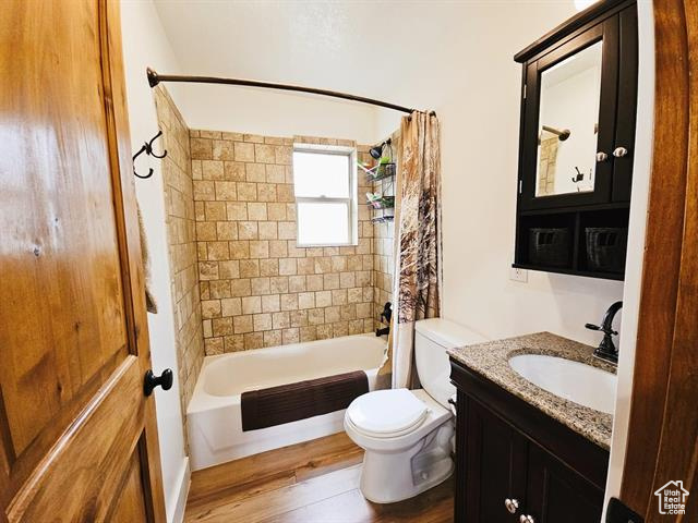 Full bath featuring toilet, shower / bath combo, vanity, and wood finished floors