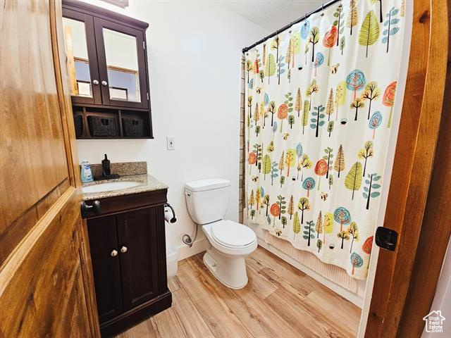 Bathroom with toilet, wood finished floors, vanity, and shower / bath combo