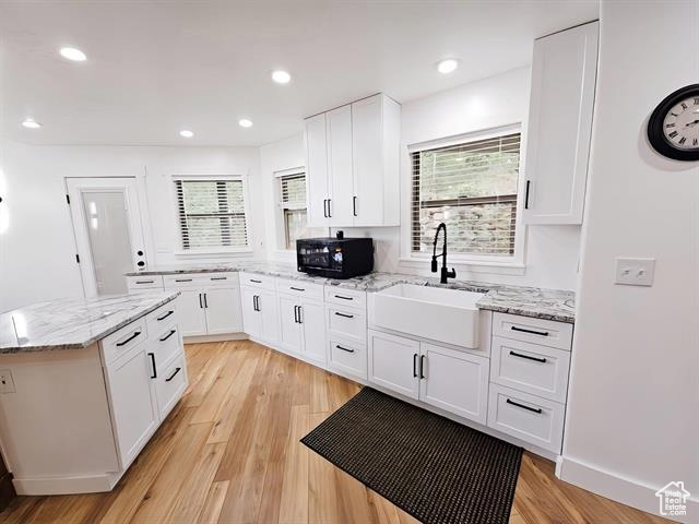 Kitchen with a sink, black microwave, white cabinetry, light wood-type flooring, and recessed lighting
