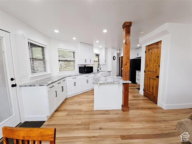 Kitchen featuring black microwave, a kitchen island, white cabinetry, light wood-type flooring, and recessed lighting