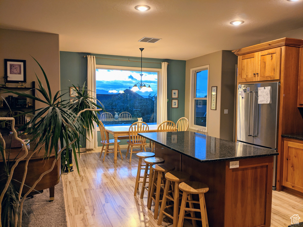 Kitchen with high quality fridge, light wood-type flooring, a chandelier, a breakfast bar area, and a center island