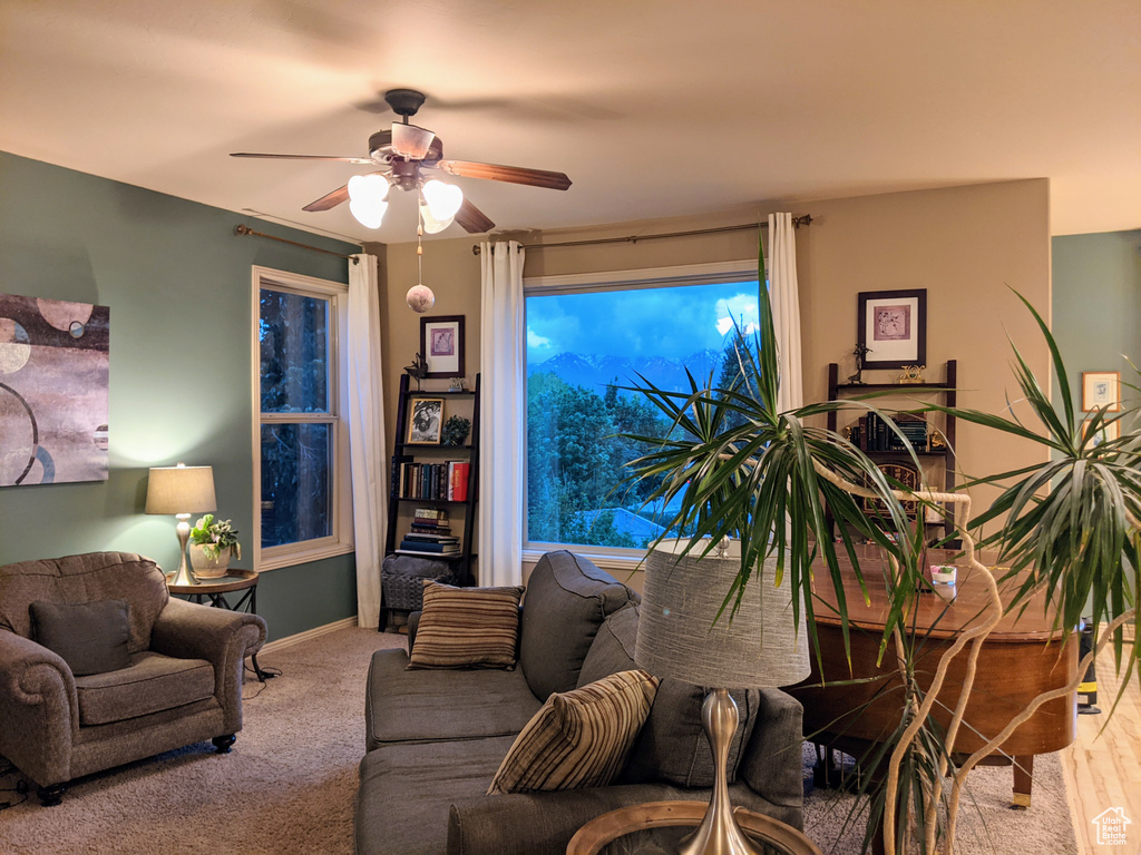 Carpeted living area featuring ceiling fan and baseboards