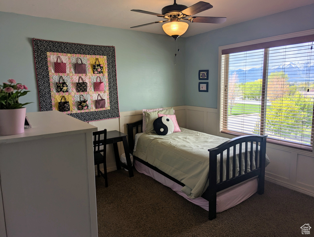 Carpeted bedroom featuring a wainscoted wall, a decorative wall, and ceiling fan