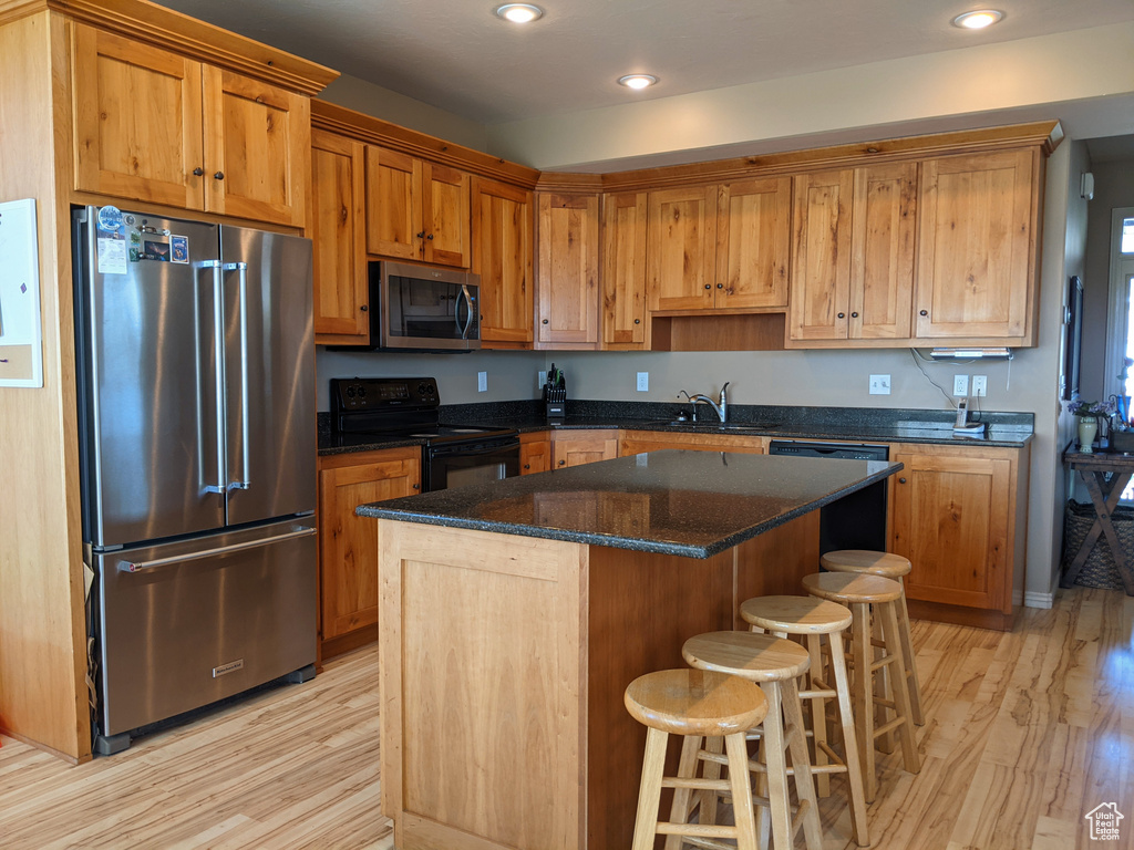 Kitchen featuring appliances with stainless steel finishes, light wood finished floors, a breakfast bar, a center island, and recessed lighting