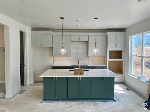 Kitchen with green cabinetry, baseboards, tasteful backsplash, a center island with sink, and recessed lighting