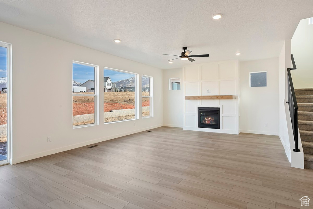 Unfurnished living room with stairs, a ceiling fan, light wood-type flooring, a large fireplace, and recessed lighting