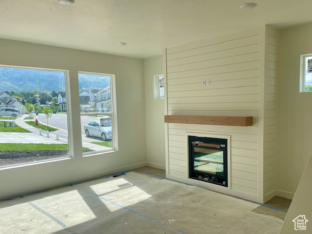 Unfurnished living room with plenty of natural light, a glass covered fireplace, and baseboards