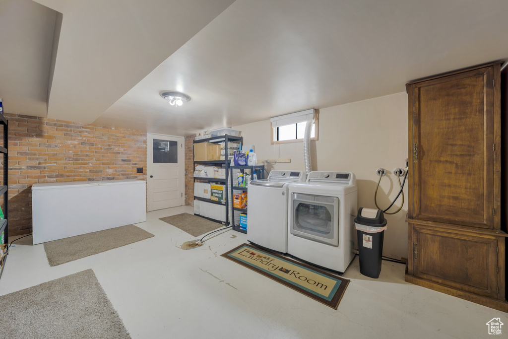 Clothes washing area with independent washer and dryer, electric panel, and brick wall