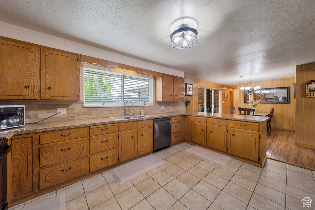Kitchen featuring stainless steel microwave, dishwashing machine, a sink, brown cabinetry, and backsplash