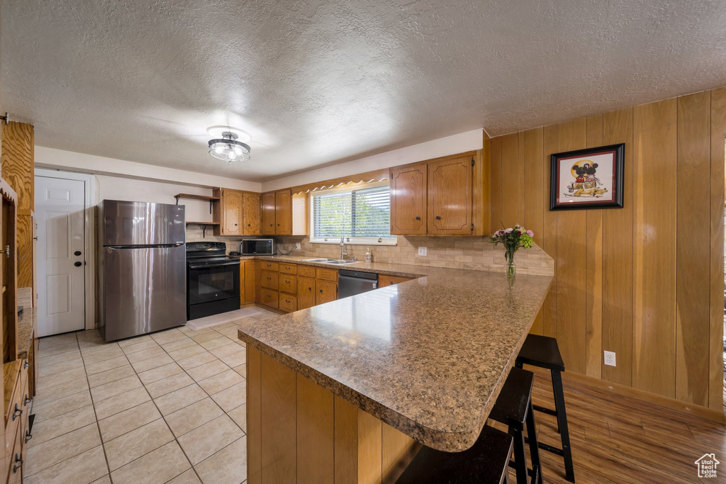 Kitchen featuring stainless steel appliances, a sink, a peninsula, brown cabinets, and a textured ceiling