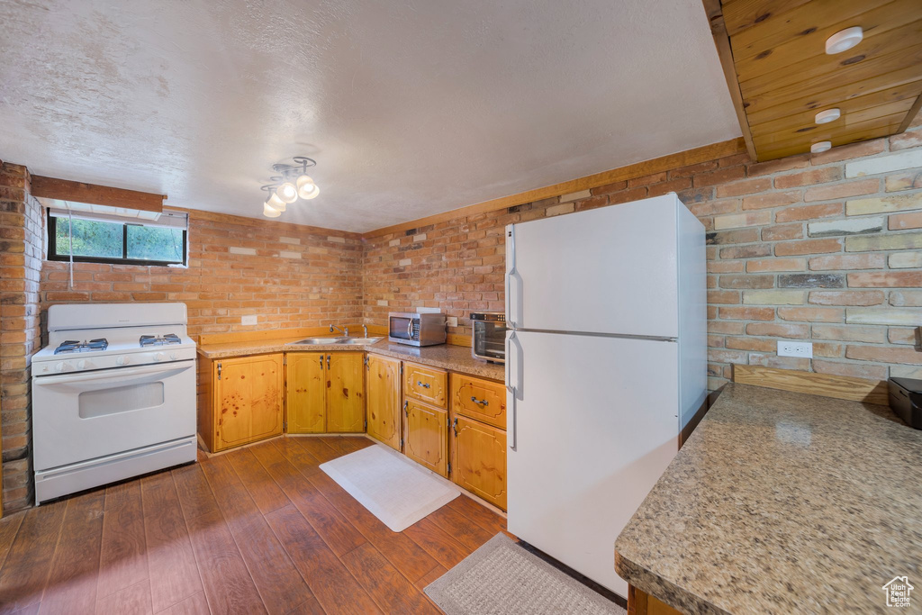 Kitchen featuring white appliances, brick wall, dark wood-style floors, a sink, and light countertops