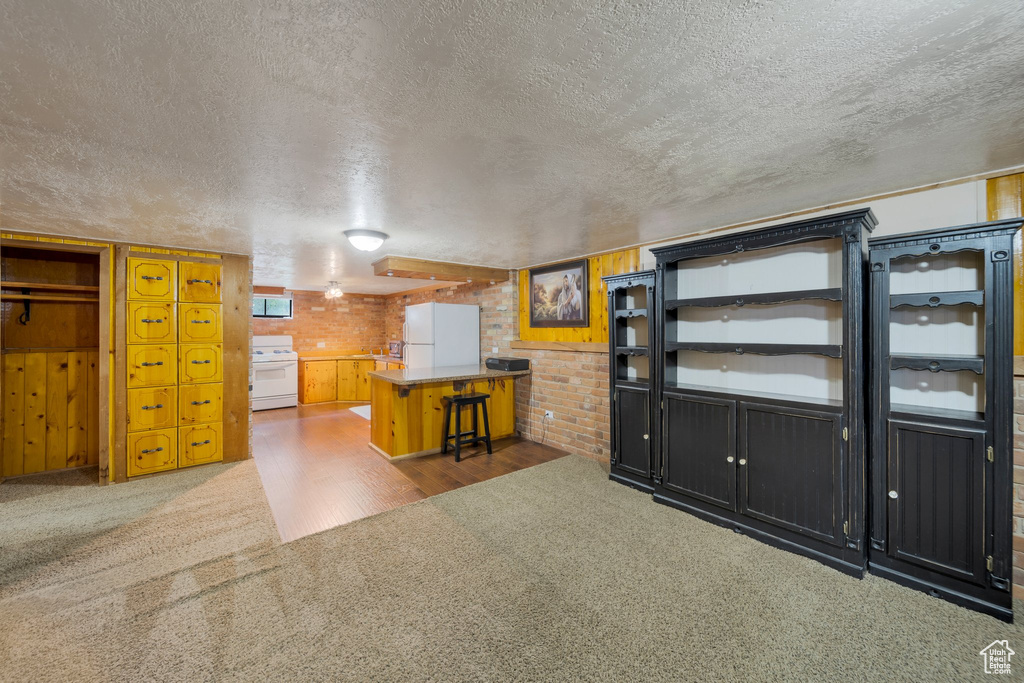 Kitchen featuring white appliances, a textured ceiling, carpet floors, and brick wall