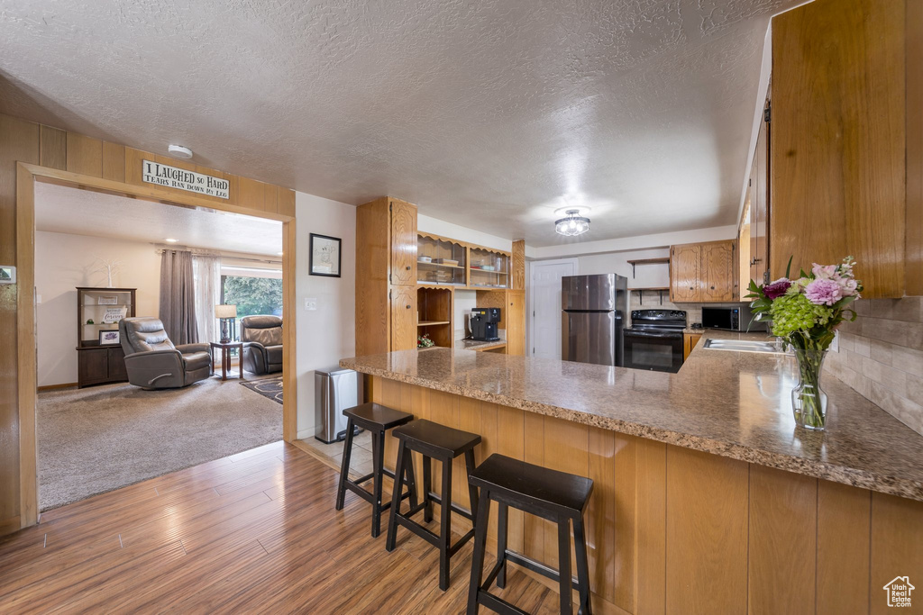 Kitchen with stainless steel appliances, light wood-style flooring, a textured ceiling, a peninsula, and light stone counters