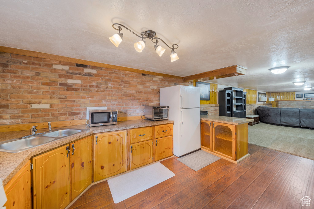 Kitchen with a sink, stainless steel microwave, freestanding refrigerator, dark wood finished floors, and brick wall